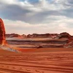 A wide Panorama of El Agabat Valley in the White Desert, showing large reddish and white rock formations against a sky with dramatic clouds.