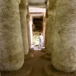 Rock-cut columns lining a passage, with a lone figure at the brightly lit end of a burial chamber at Amarna.