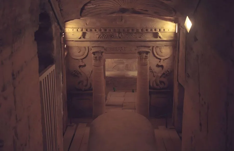 A dark, atmospheric photo of the inner chambers of the Roman Burial place Catacomb Of Kom El Shoqafa, showing a sculpted stone tomb with elaborate Egyptian and Greco-Roman decorative elements.