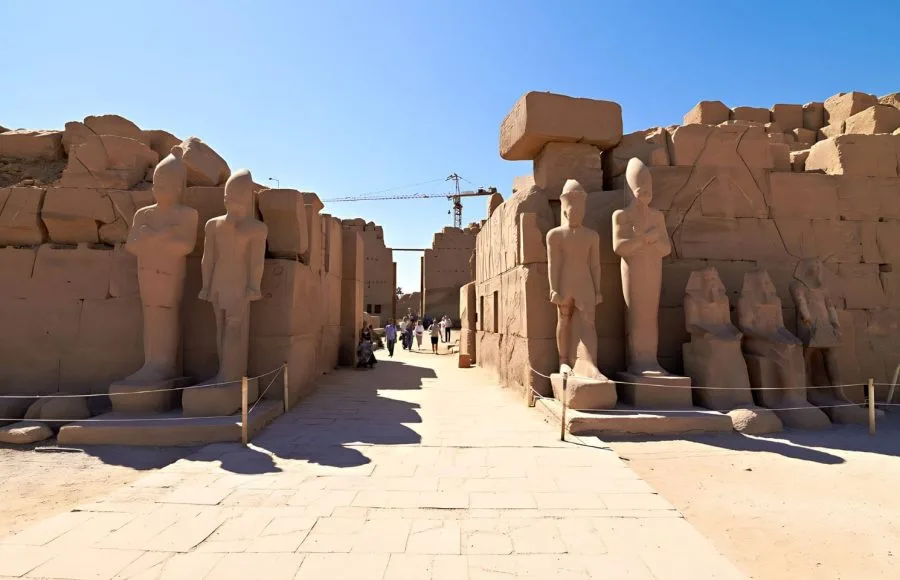 The weathered stone statues and monumental pylons marking the entrance to the Ruins Of Karnak Temple in Luxor, Egypt, under a clear blue sky.