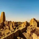 A wide view of the crumbling mud-brick Ruins Of The Amun Oracle Temple In Siwa Oasis, showing a prominent, tall, tower-like structure rising from the complex.