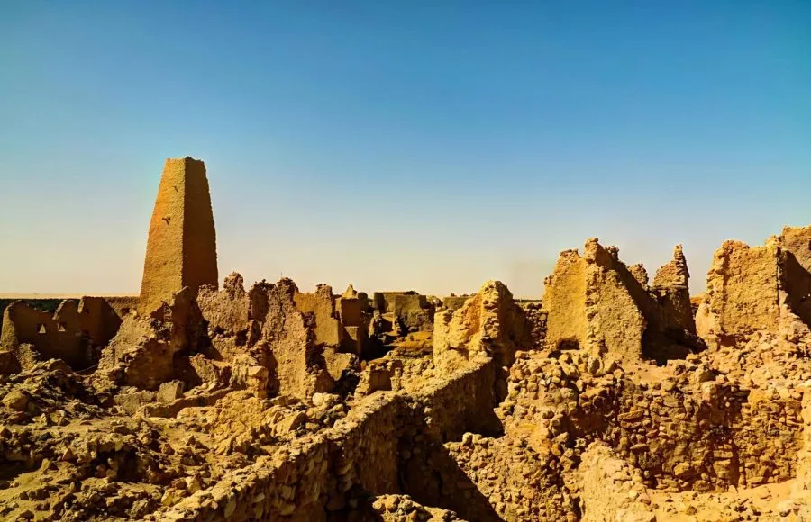A wide view of the crumbling mud-brick Ruins Of The Amun Oracle Temple In Siwa Oasis, showing a prominent, tall, tower-like structure rising from the complex.