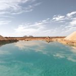 Wide panoramic view of a bright turquoise Salt Lake of Siwa, reflecting the sky and clouds, with banks of white and tan salt deposits surrounding the water.