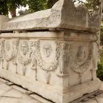 Elaborately carved stone sarcophagus featuring masks and garlands outside the Catacombs of Kom El Shoqafa in Alexandria, Egypt.