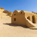 Small, earth-toned, arched building contrasting with the desert landscape and eroded cliffs at Wadi El Hitan.