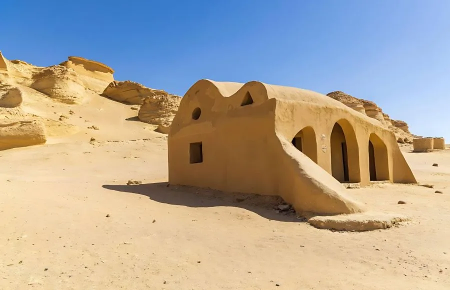 Small, earth-toned, arched building contrasting with the desert landscape and eroded cliffs at Wadi El Hitan.