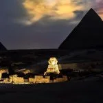 Wide view of the Sphinx and Pyramids under a dramatic orange and purple twilight sky.