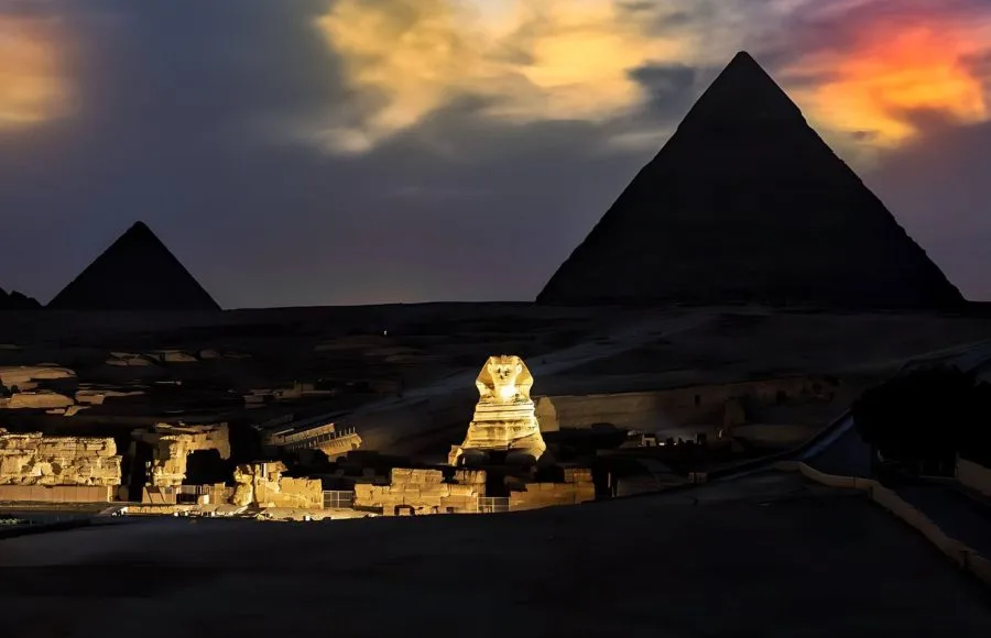 Wide view of the Sphinx and Pyramids under a dramatic orange and purple twilight sky.