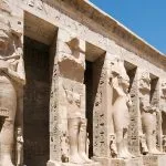 A row of large, rock-cut statues of Ramesses III lining the entrance to the inner court at the Statues in the Court of the Temple of Medinet Habu in Luxor, Egypt.