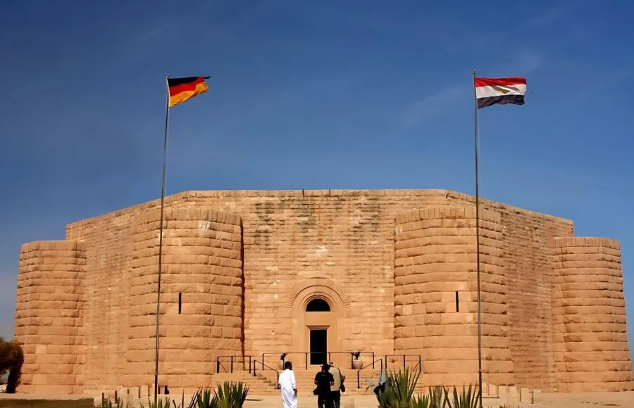 Exterior view of the imposing German War Graves Memorial in El Alamein, Egypt, featuring the German and Egyptian flags.