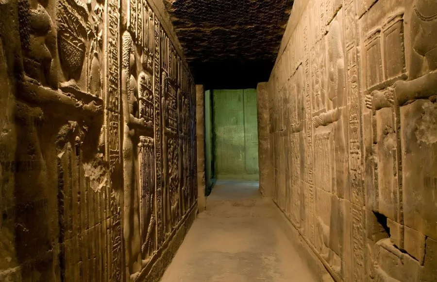A detailed view of a narrow, ancient passage lined with deep, complex Hieroglyphics Carving Inside Dendera Temple, illuminated by soft interior light.
