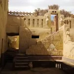 Interior courtyard view of the Badr Museum and house in Farafra, Egypt, featuring traditional mud-brick architecture decorated with large relief carvings of a town and figures.