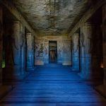 The dimly lit interior of The Large Hall Of The Temple Of Hathor At Abu Simbel, showing large columns, carved walls, and a wooden pathway leading deeper into the temple.