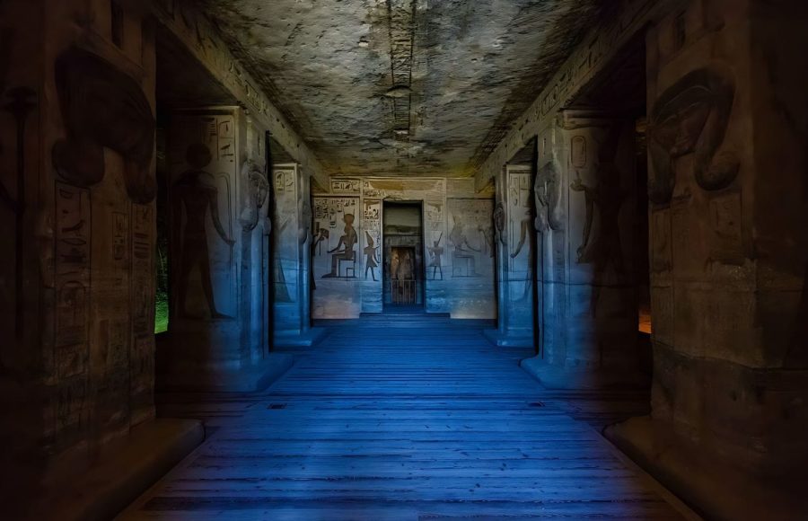 The dimly lit interior of The Large Hall Of The Temple Of Hathor At Abu Simbel, showing large columns, carved walls, and a wooden pathway leading deeper into the temple.