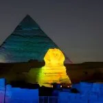 The Great Sphinx and Pyramid glowing with vibrant green and blue lights at night.