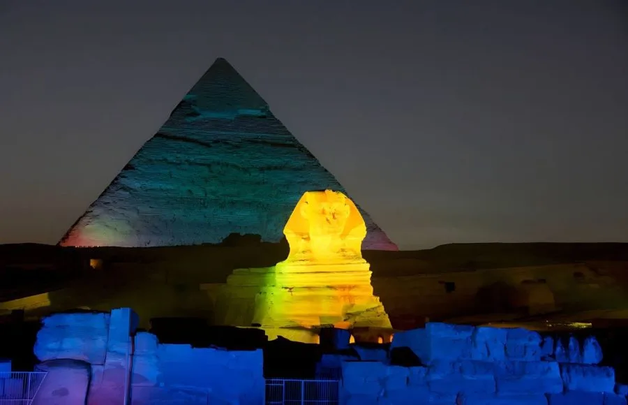 The Great Sphinx and Pyramid glowing with vibrant green and blue lights at night.