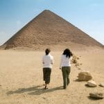 Tourists walking toward the massive Red Pyramid of Dahshur, a remarkable ancient Egyptian monument in the desert.