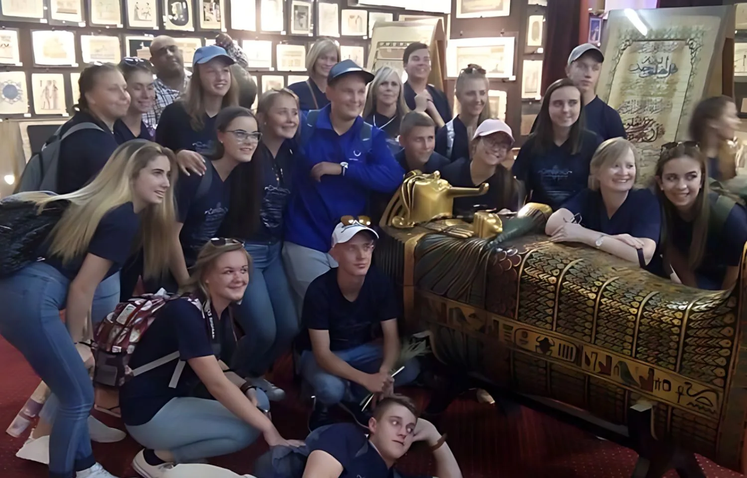 A group of tourists posing with a golden Egyptian sarcophagus replica at the Egypt Papyrus Institute.