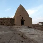 An ancient, conical mud-brick house or structure in the historical section of the Town of Bawiti, Bahariya Oasis, sitting on a rocky outcrop surrounded by other traditional buildings.