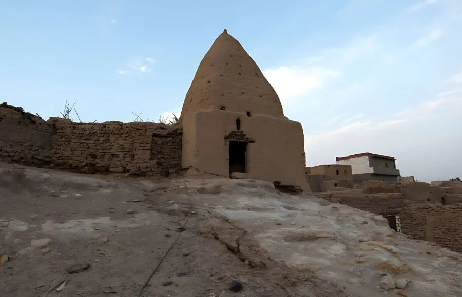 An ancient, conical mud-brick house or structure in the historical section of the Town of Bawiti, Bahariya Oasis, sitting on a rocky outcrop surrounded by other traditional buildings.
