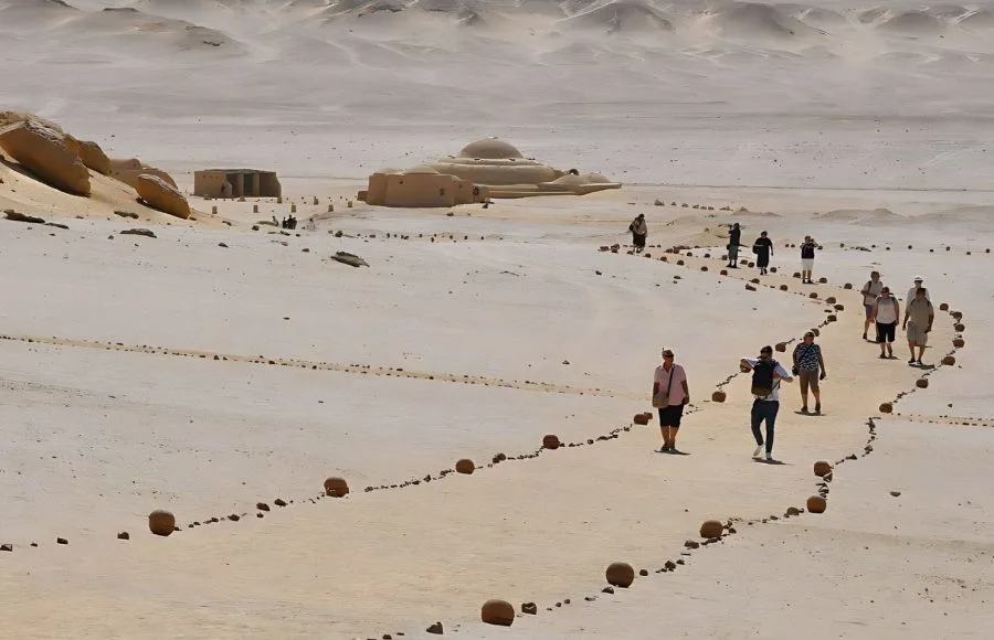 Visitors walking on a path marked by stones toward the desert museum buildings at Wadi El Hitan.