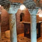 The dimly lit, ancient stone arches and pillars of the underground View Of The Crypt Abu Sergius Church, showing rough-hewn columns and simple steps leading down.