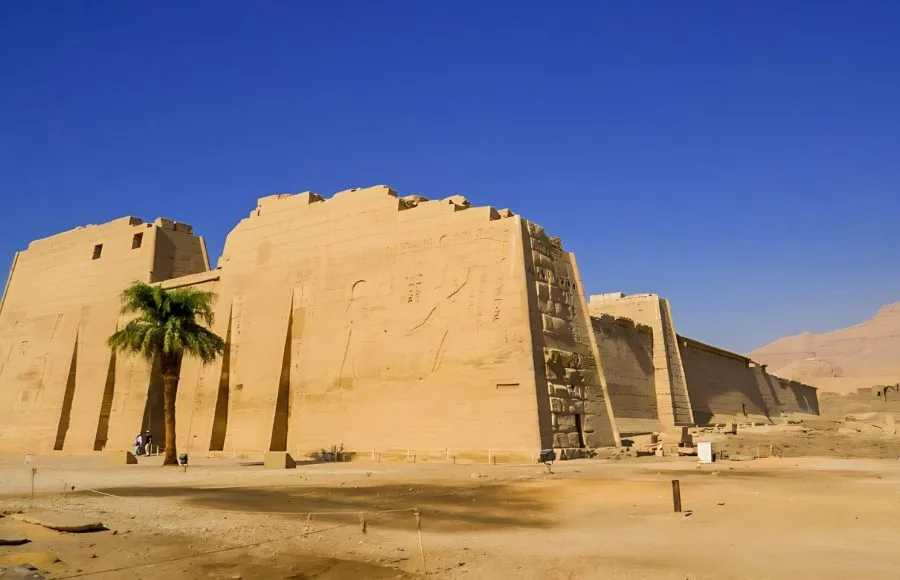 The colossal exterior walls of the View of the Medinet Habu Temple in Luxor, showing the side perspective of the ancient Egyptian structure against a clear blue sky.