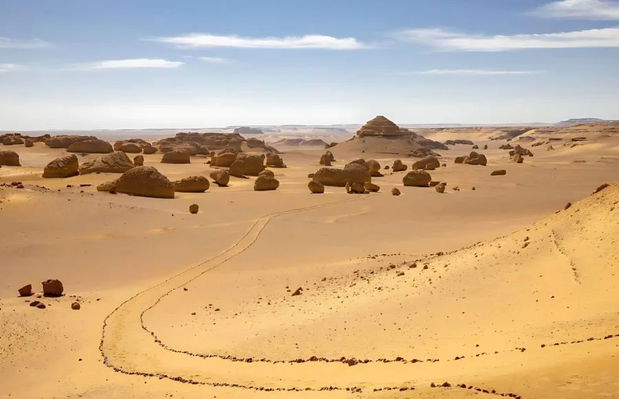 Wadi Al-Hitan trail winding through the Western Desert of Egypt's striking rock formations and golden sand dunes.