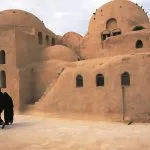 Two Coptic Orthodox nuns walk past the ancient, domed Monastery of Saint Bishoy (Deir Amba Bishoy) in Wadi El Natrun, Egypt.