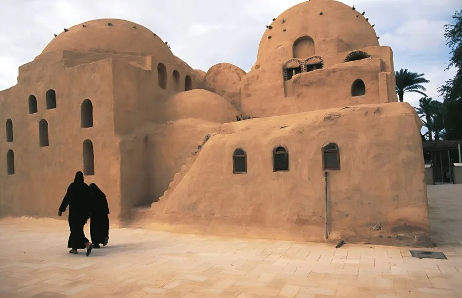 Two Coptic Orthodox nuns walk past the ancient, domed Monastery of Saint Bishoy (Deir Amba Bishoy) in Wadi El Natrun, Egypt.