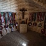 The solemn room dedicated to German general Erwin Rommel at the German cemetery in El Alamein, featuring a stone memorial, crucifix, military wreaths, and ribbons displayed on the curved brick walls.