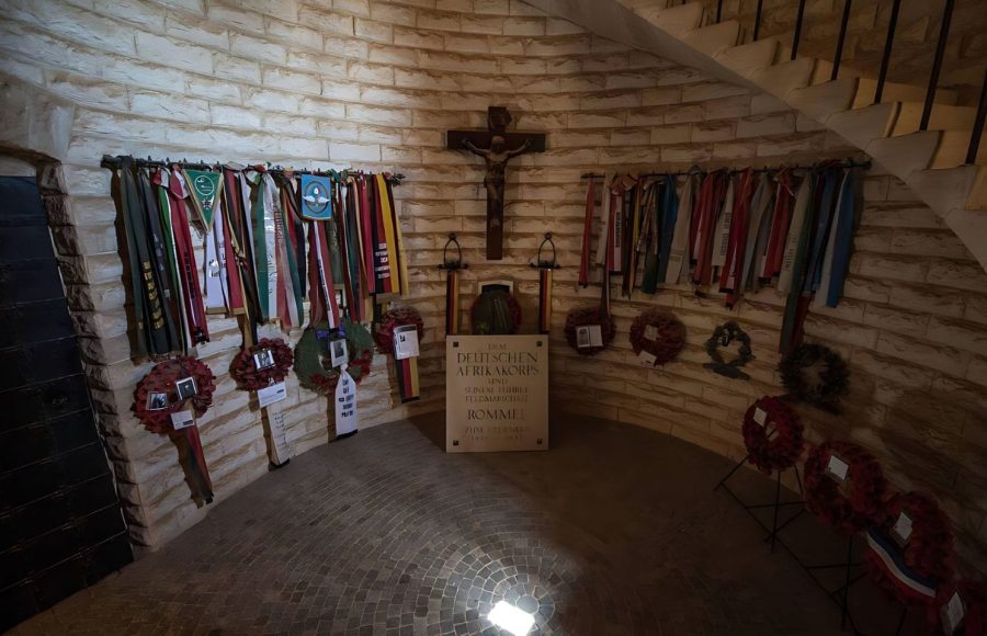 The solemn room dedicated to German general Erwin Rommel at the German cemetery in El Alamein, featuring a stone memorial, crucifix, military wreaths, and ribbons displayed on the curved brick walls.