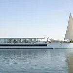 A white luxury Dahabiya sailing vessel with large sails on the Nile River, surrounded by water and lush green riverbanks in Egypt.