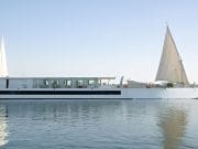 A white luxury Dahabiya sailing vessel with large sails on the Nile River, surrounded by water and lush green riverbanks in Egypt.