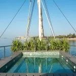 Sun deck of the Kazazian Berge Dahabiya, a luxury Nile cruise ship, featuring a rectangular plunge pool with jets and lush green riverbanks in the background.