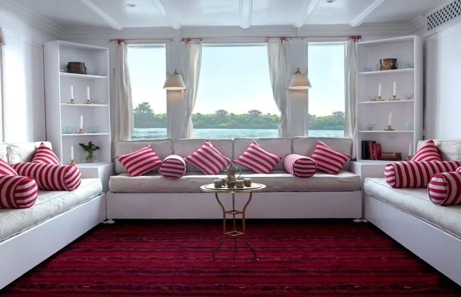 Interior lounge of the Lazuli Abydos Dahabiya Nile Cruise with white sofas, white shelving, and striking red and white striped cushions.
