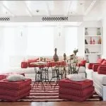 A cozy, well-lit lounge area on the Lazuli Abydos Dahabiya Nile Cruise boat, featuring vibrant red and white striped cushions, dark wood furniture, and a rug with similar patterns.