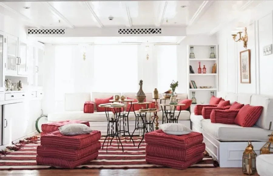 A cozy, well-lit lounge area on the Lazuli Abydos Dahabiya Nile Cruise boat, featuring vibrant red and white striped cushions, dark wood furniture, and a rug with similar patterns.