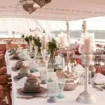 A dining table on the upper deck of the Lazuli Abydos Dahabiya Nile Cruise boat, set with fine china and silverware, ready for a meal with a river view.