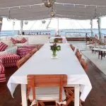 Sun deck of the Lazuli Abydos Dahabiya Nile Cruise boat, featuring a set dining table, lounge chairs, and views of the Nile.