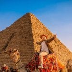 Tourist on a camel in front of the massive Great Giza Pyramid.