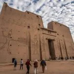 A group of tourists approaches the massive, awe-inspiring entrance of the Edfu Temple in Egypt