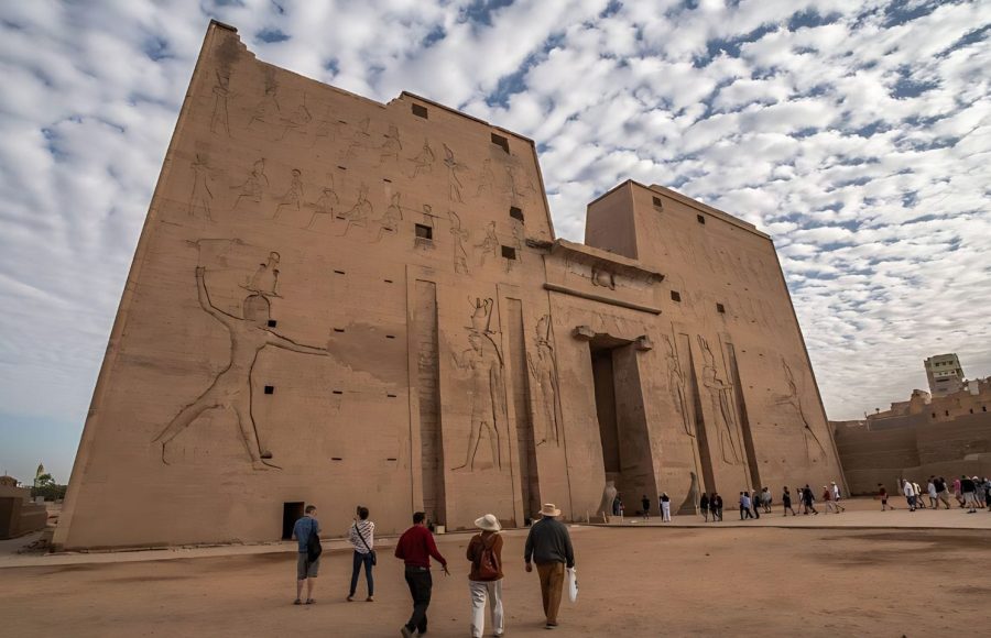 A group of tourists approaches the massive, awe-inspiring entrance of the Edfu Temple in Egypt