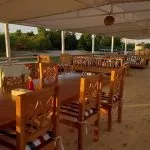 An outdoor dining deck on a cruise ship with wooden tables, chairs, and a view of the water and shore.