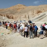 A large group of tourists queues in the desert landscape of the Valley of the Kings in Luxor, waiting to enter one of the ancient tombs.