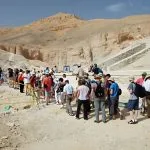 A large group of tourists queues in the desert landscape of the Valley of the Kings in Luxor, waiting to enter one of the ancient tombs.