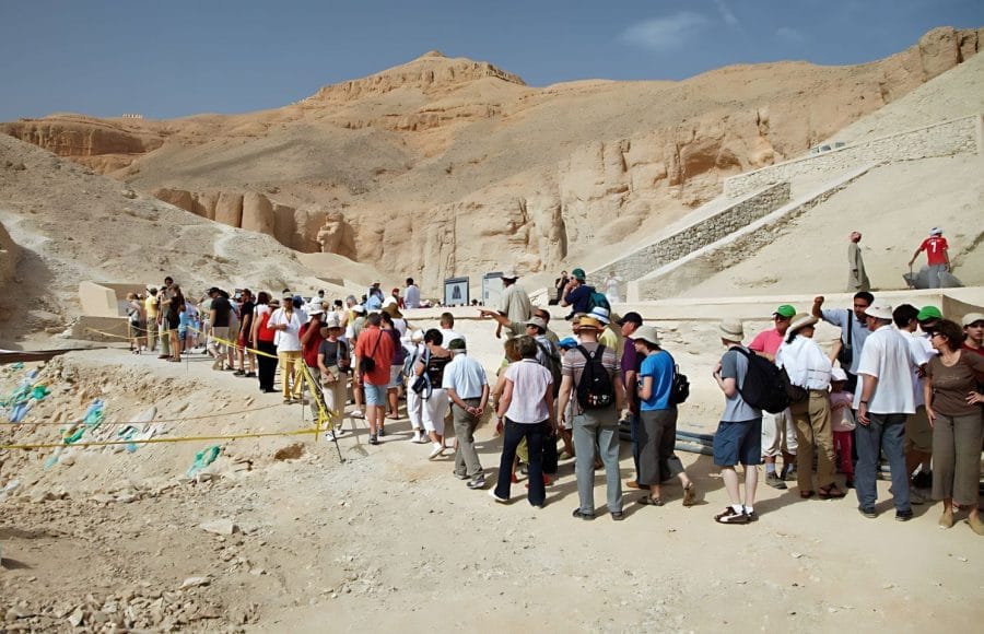A large group of tourists queues in the desert landscape of the Valley of the Kings in Luxor, waiting to enter one of the ancient tombs.