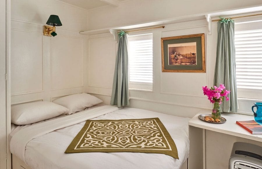 Cabin interior aboard the Lazuli Gordon Pacha Dahabiya Nile Cruise with a bed, two windows, and a small table.