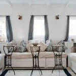 A bright, elegantly decorated living room suite on a Nile cruise boat with white sofas, blue cushions, and small iron side tables.