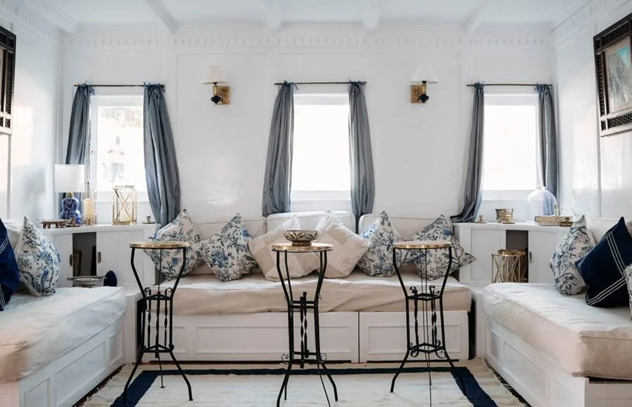 A bright, elegantly decorated living room suite on a Nile cruise boat with white sofas, blue cushions, and small iron side tables.